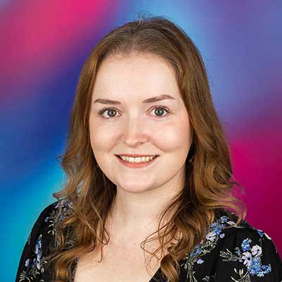 Headshot of person smiling in dark floral top with wavy shoulder length light brown hair