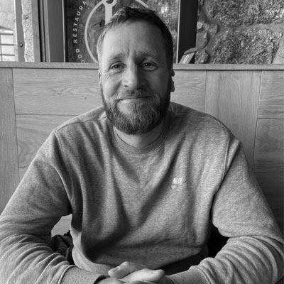 Person with beard and short dark hair wearing jumper smiling at camera