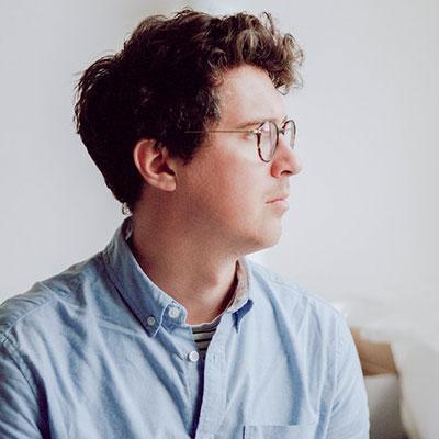 Young man with brown hair, glasses and wearing a light blue shirt.