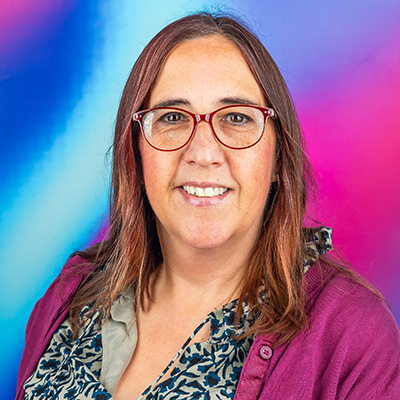 A Bath Spa governor sits in front of a colourful blue and purple background