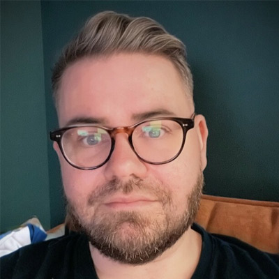 Headshot of someone with short light hair wearing glasses in dark t-shirt