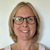 Headshot of someone with shoulder-length blonde hair and glasses, smiling