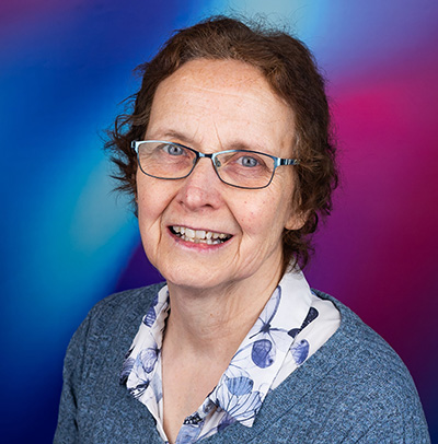 A Bath Spa University staff member in front a background of a blue and purple background.