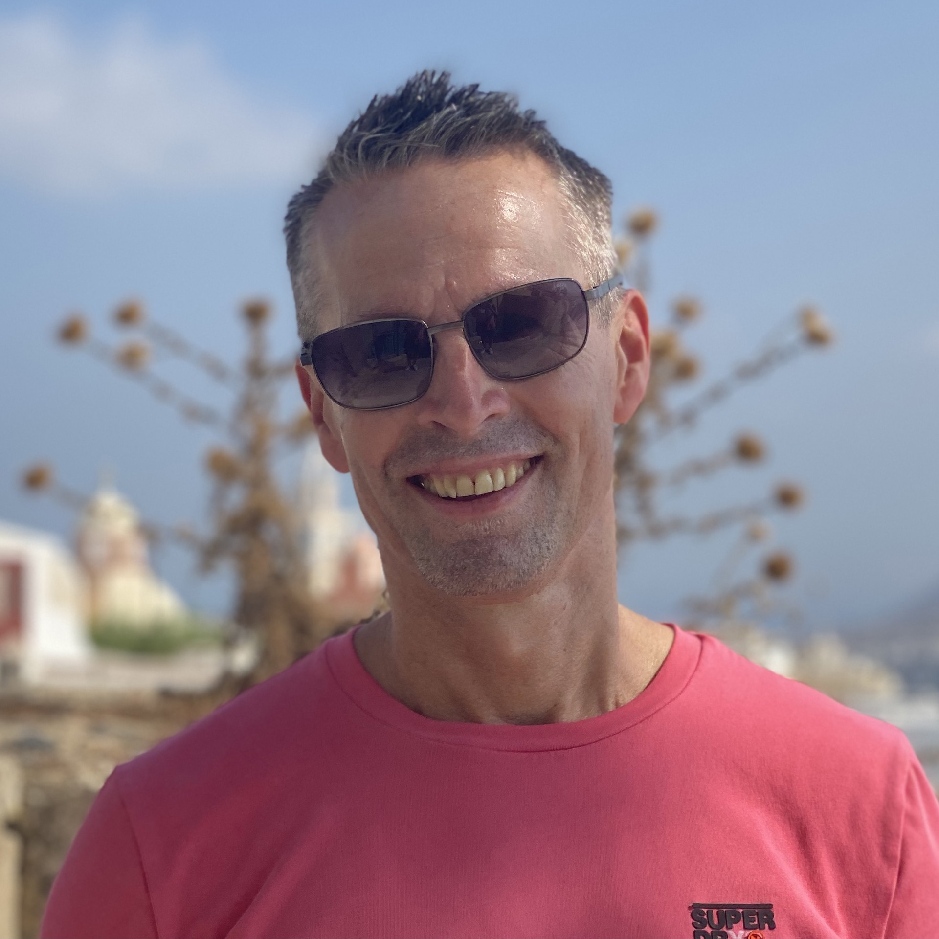 A profile picture of a man smiling in sunglasses and a pink T-shirt.