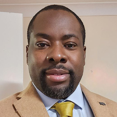 A profile picture of a Bath Spa University staff member in a suit against a beige background.