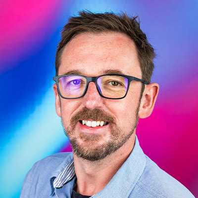 Headshot of someone with short hair, glasses and blue shirt