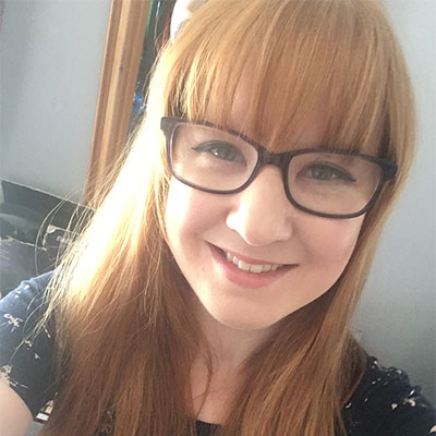 Young woman with light ginger hair and a blunt fringe wearing round black-rimmed glasses.