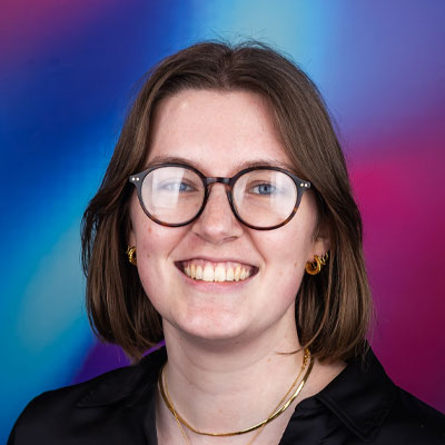Headhsot of someone with shoulder-length brown hair wearing jewellery smiling