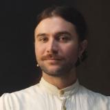 Headshot of someone with beard and long hair tied back in white shirt with grandad collar