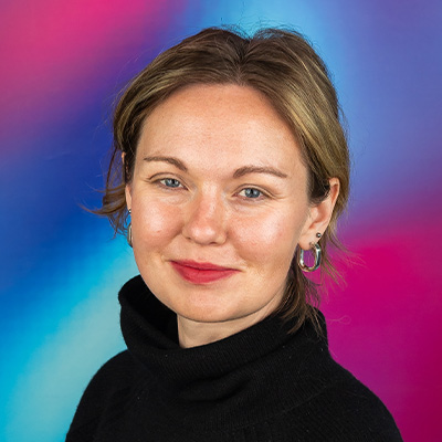 Headshot of someone with blonde hair tied back in black poloneck jumper