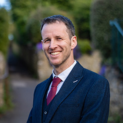 A man in a suit and red tie smiles at the camera