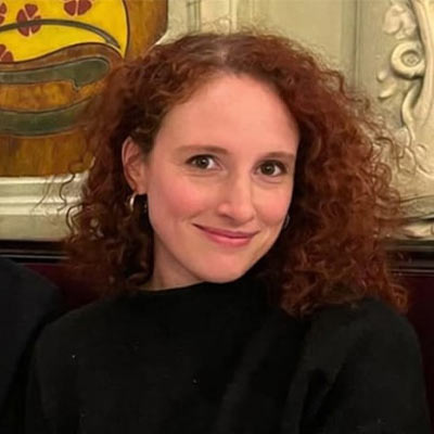 Headshot photo of someone with curly red hair in a black jumper smiling