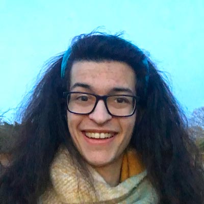 Person with long dark hair and glasses smiling at camera