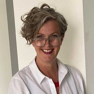 Person with short light hair and glasses smiling in white shirt