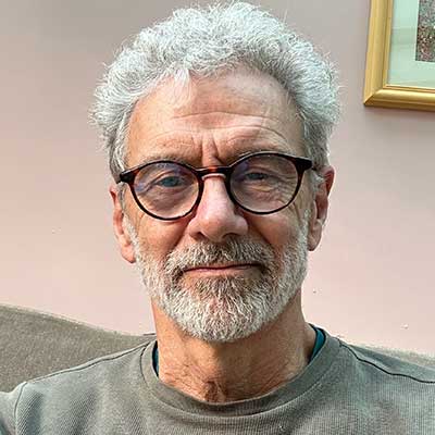 A person with grey hair and glasses smiles at the camera