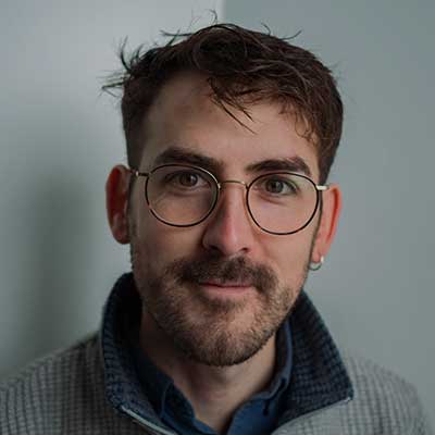 A man with short brown hair and round tortoiseshell glasses