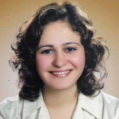 A person with brown, curly hair smiles at the camera