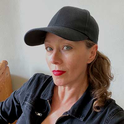 A person wearing a black denim jumpsuit and a black cap