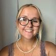 A student with blonde hair and glasses smiles at the camera