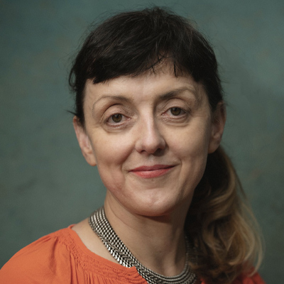 A woman with long dark hair and a fringe smiles at camera