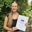 A person with long blonde hair holds her completed dissertation to show the camera