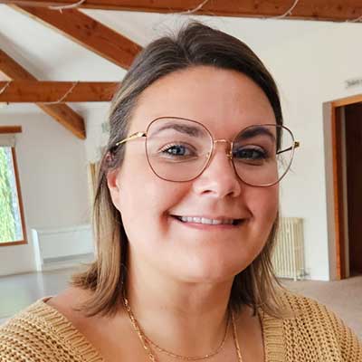 A person with brown hair and large, round  glasses smiles at the camera