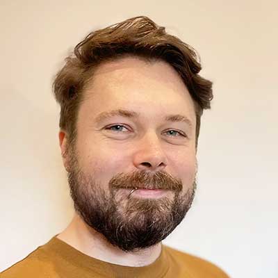 A man with brown hair and a beard smiles at the camera