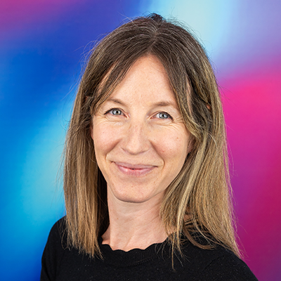 A person with shoulder-length brown hair smiles at the camera