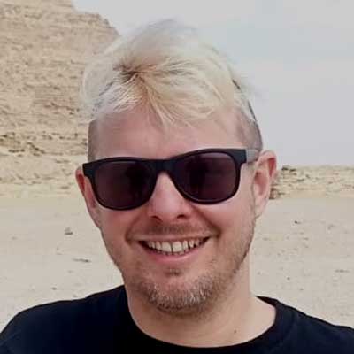 A man with blonde hair and sunglasses smiles at the camera