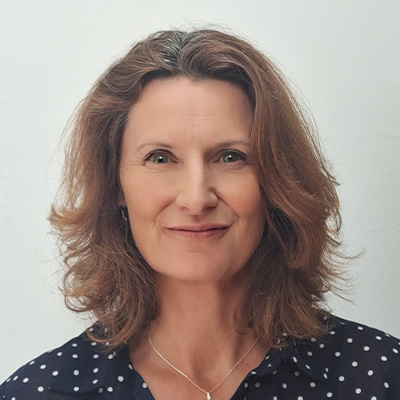 Headshot of someone with shoulder length light brown hair in spotted blouse
