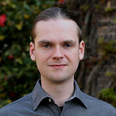 A man with slicked-back hair looks into the camera lens