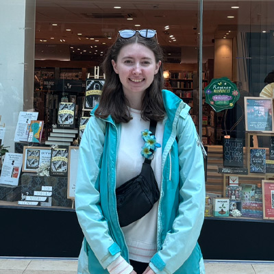 Person in blue coat smiling outside a bookshop