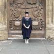 A person wearing navy graduation robes stands in front of a large ornate door outside Bath Abbey
