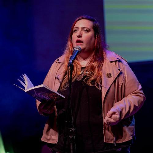 A poet on stage, reading a poem out of an open book