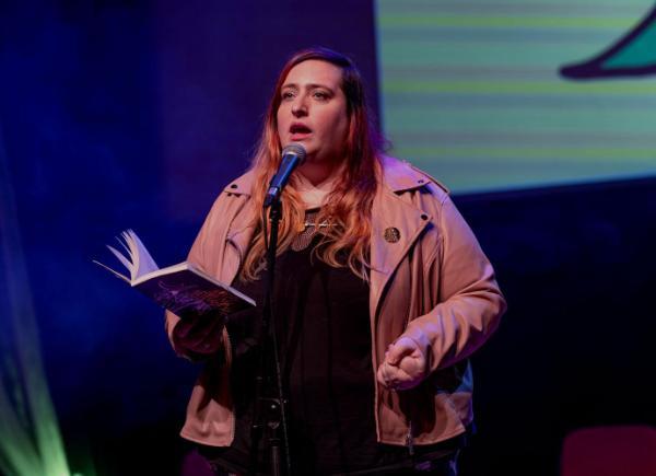 A poet on stage, reading a poem out of an open book