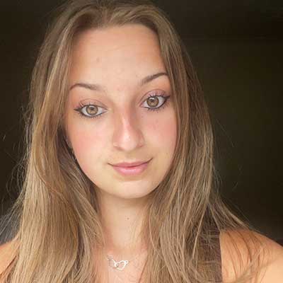 A person with long light brown hair looks at the camera