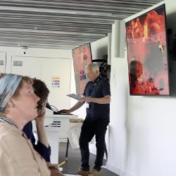 Person with short white hair giving a lecture in front of a screen