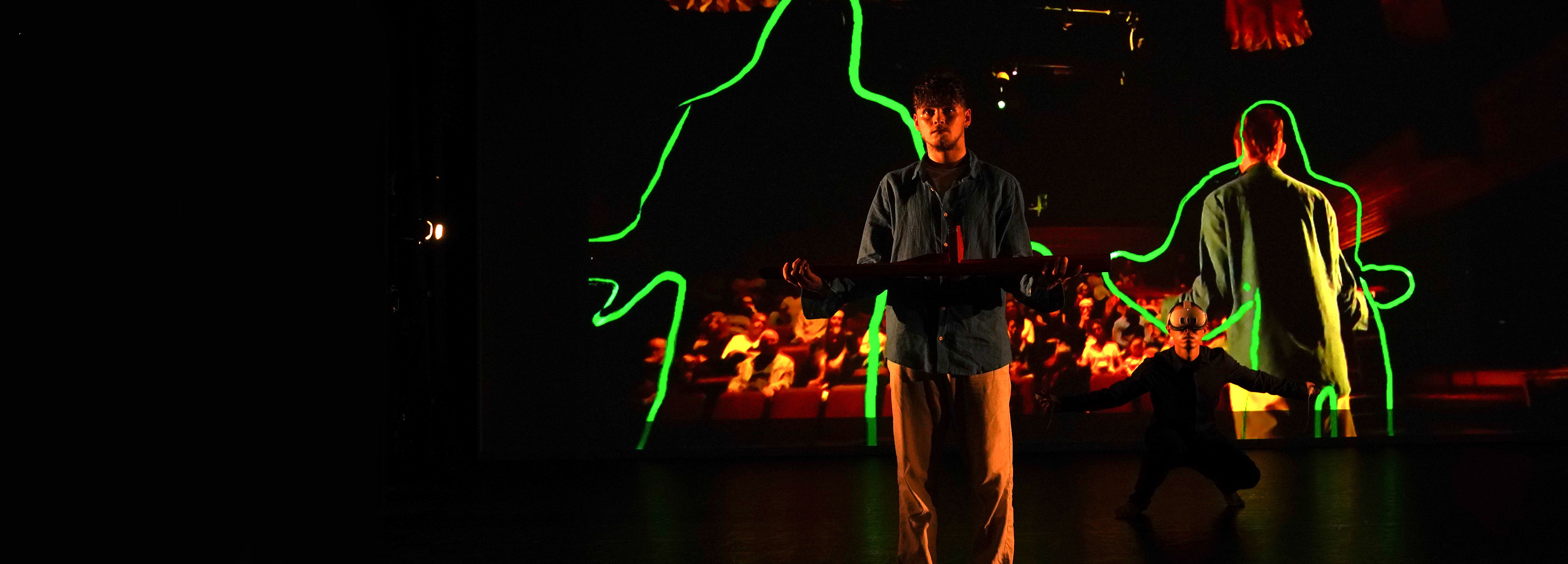 An actor on a stage in front of a screen showing the audience he is facing