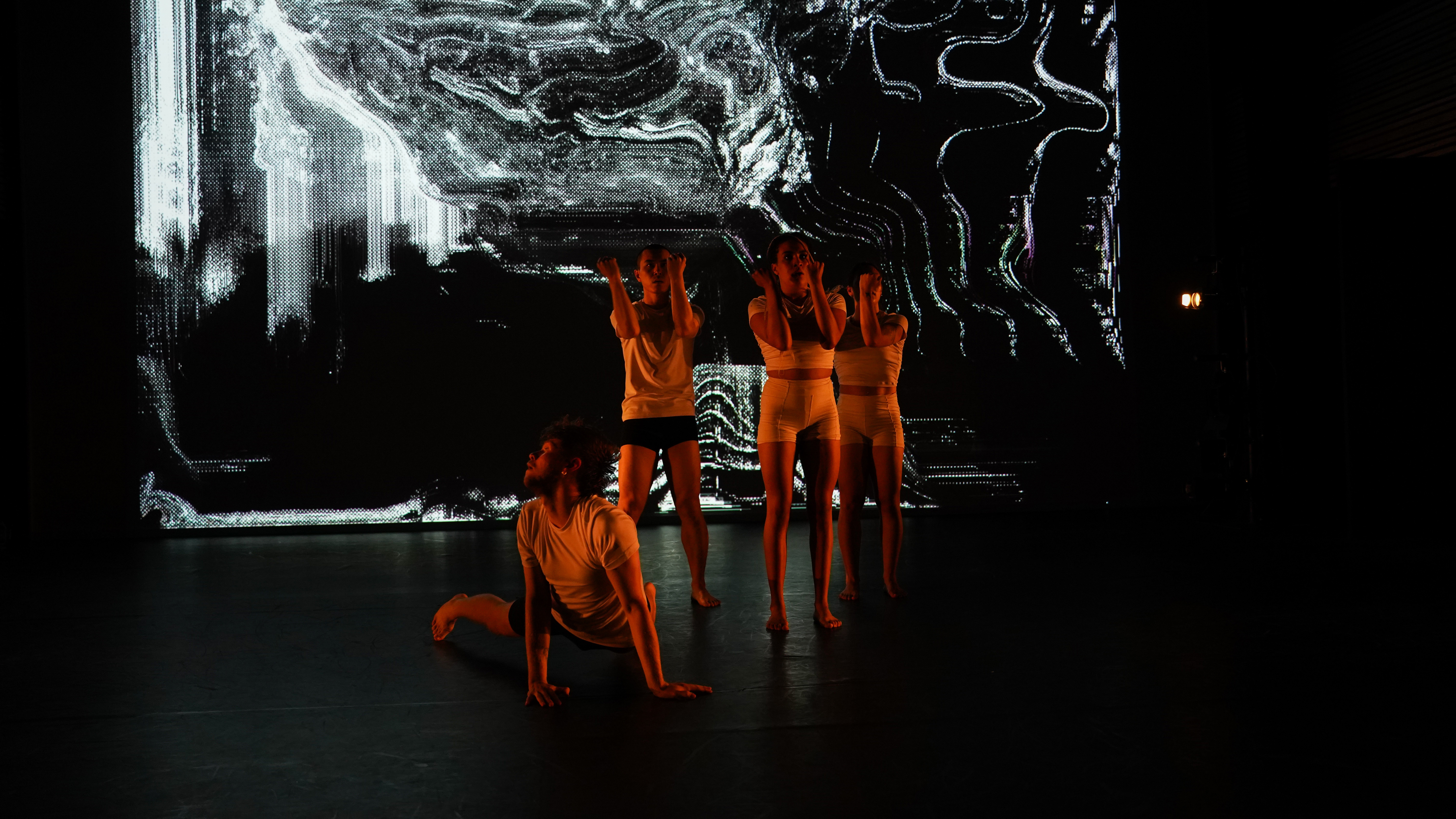 Performers huddle in front of a screen showing a scattering of white pixels on a black background