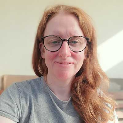 A person with long red hair and dark framed glasses