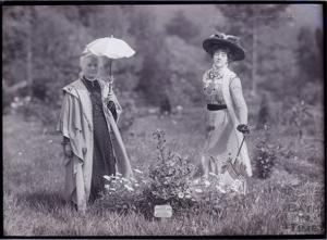 Two women one with parasol in traditional dress in a field