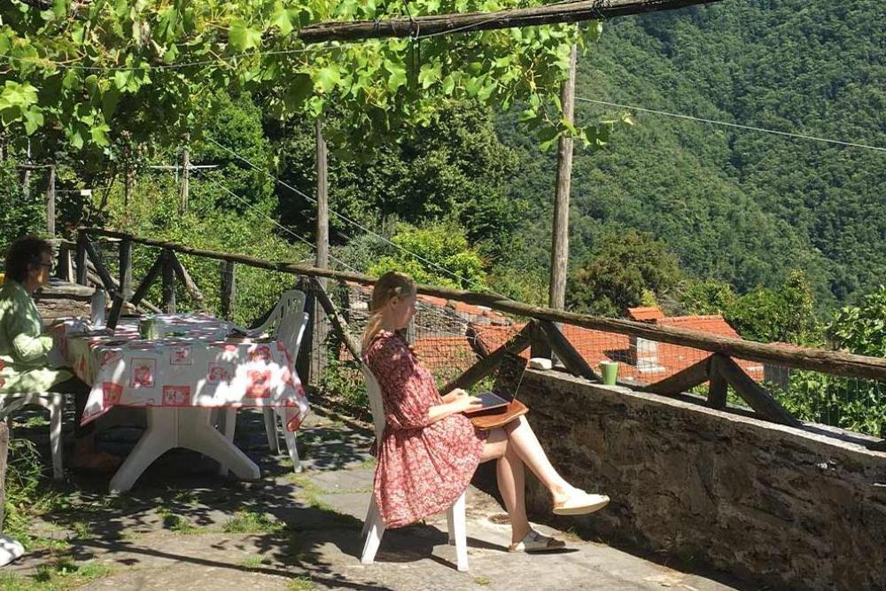 Person in long pink dress sitting writing on a terrace in leafy mountains
