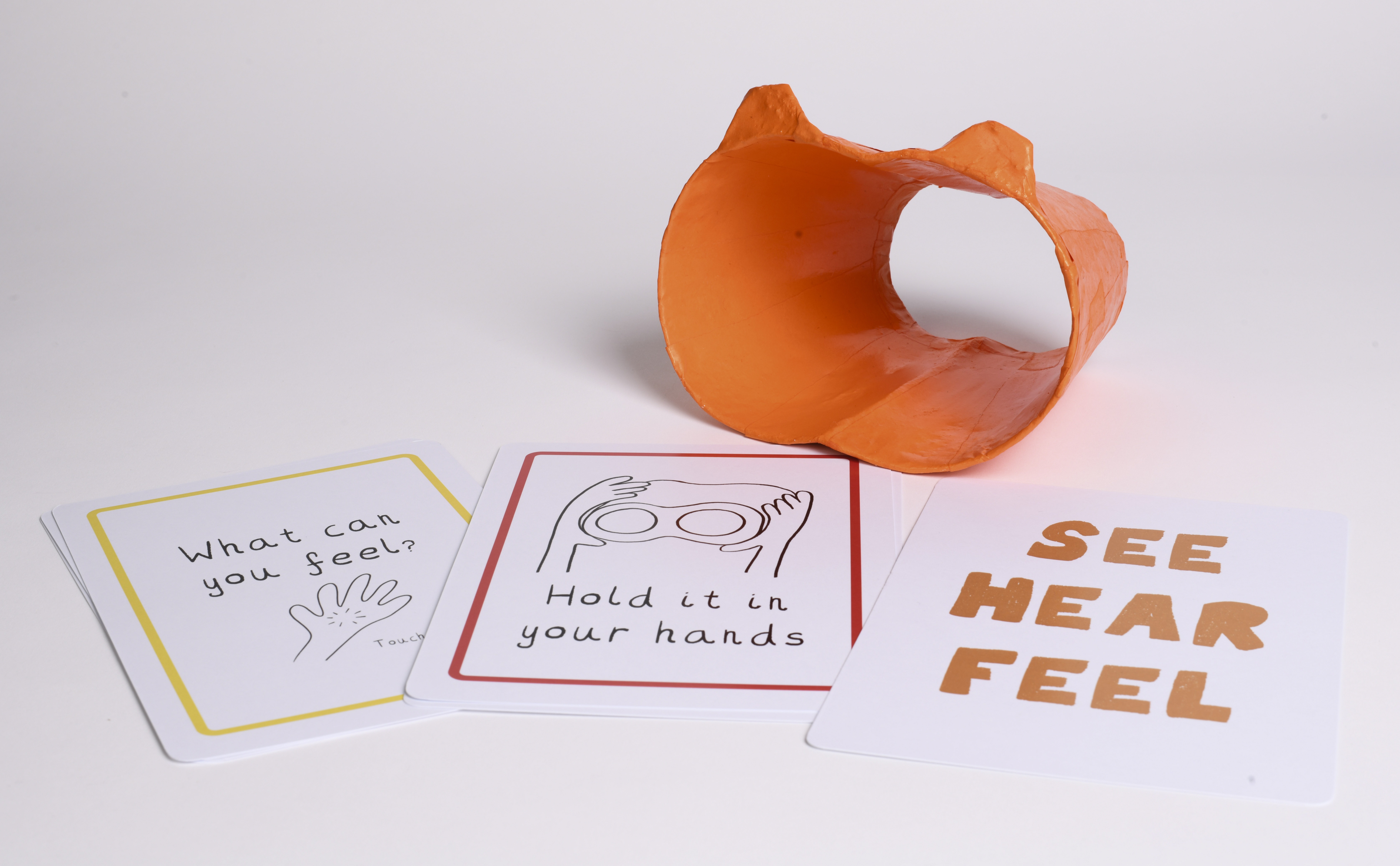 Three white cards laid on a table with an orange binocular-shaped sculpture sitting next to it