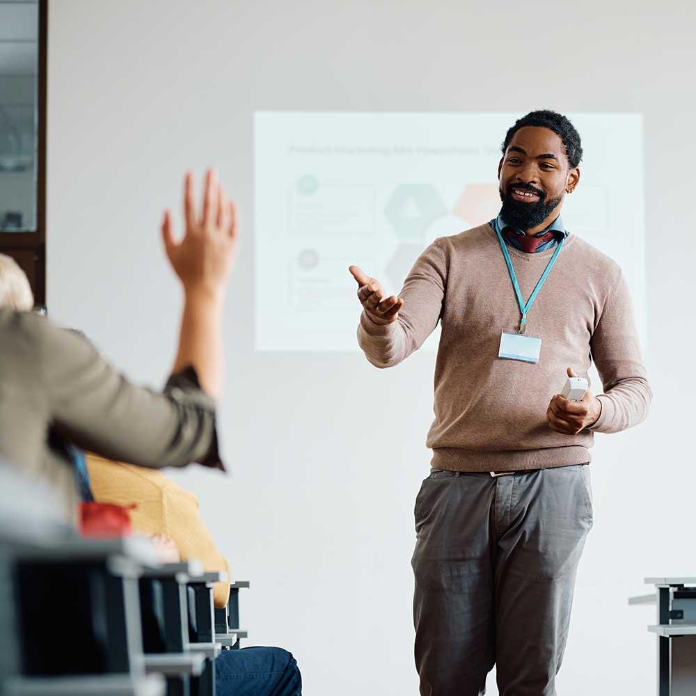A lecturer walks in front of a class and invites someone to speak