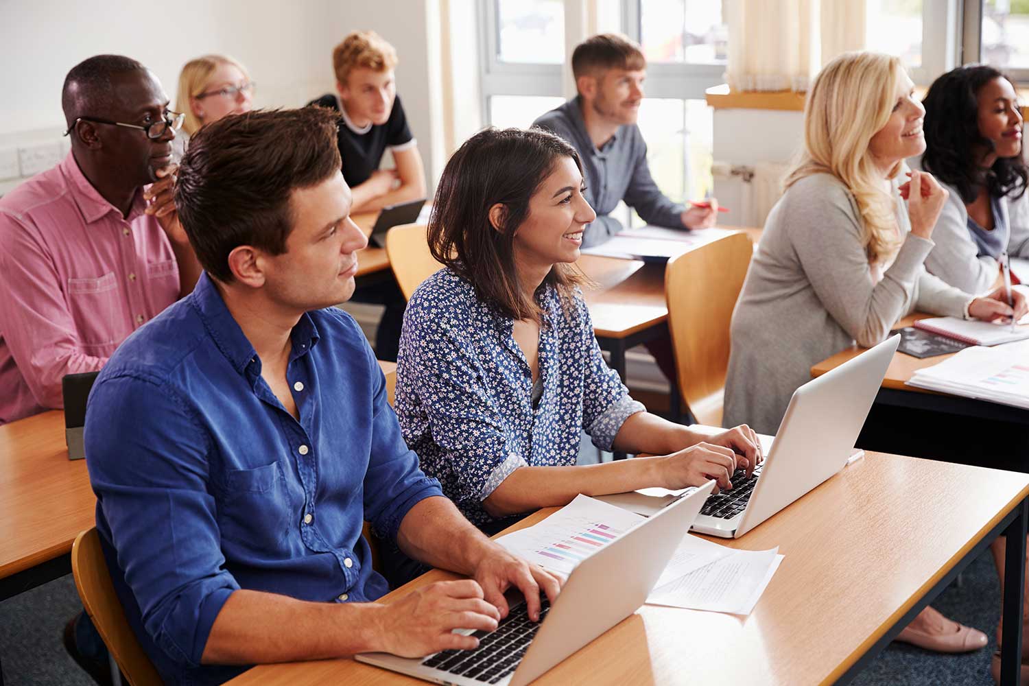 A group of adult learners sit at desks in a classroom