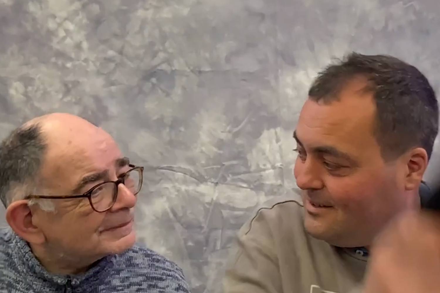 Two men smiling at one another trying on caps