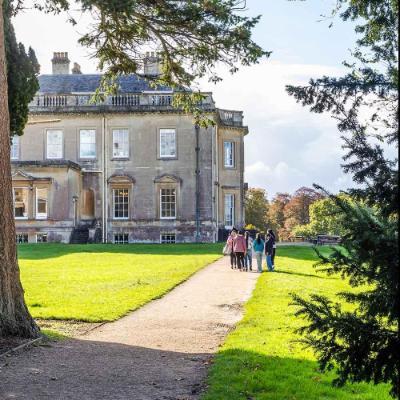 Shot of Main House through trees with students on path