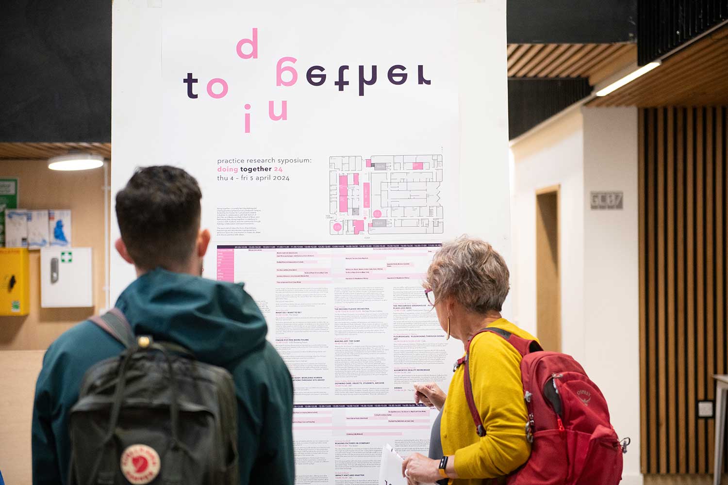 Two people look at a large poster displaying a timetable