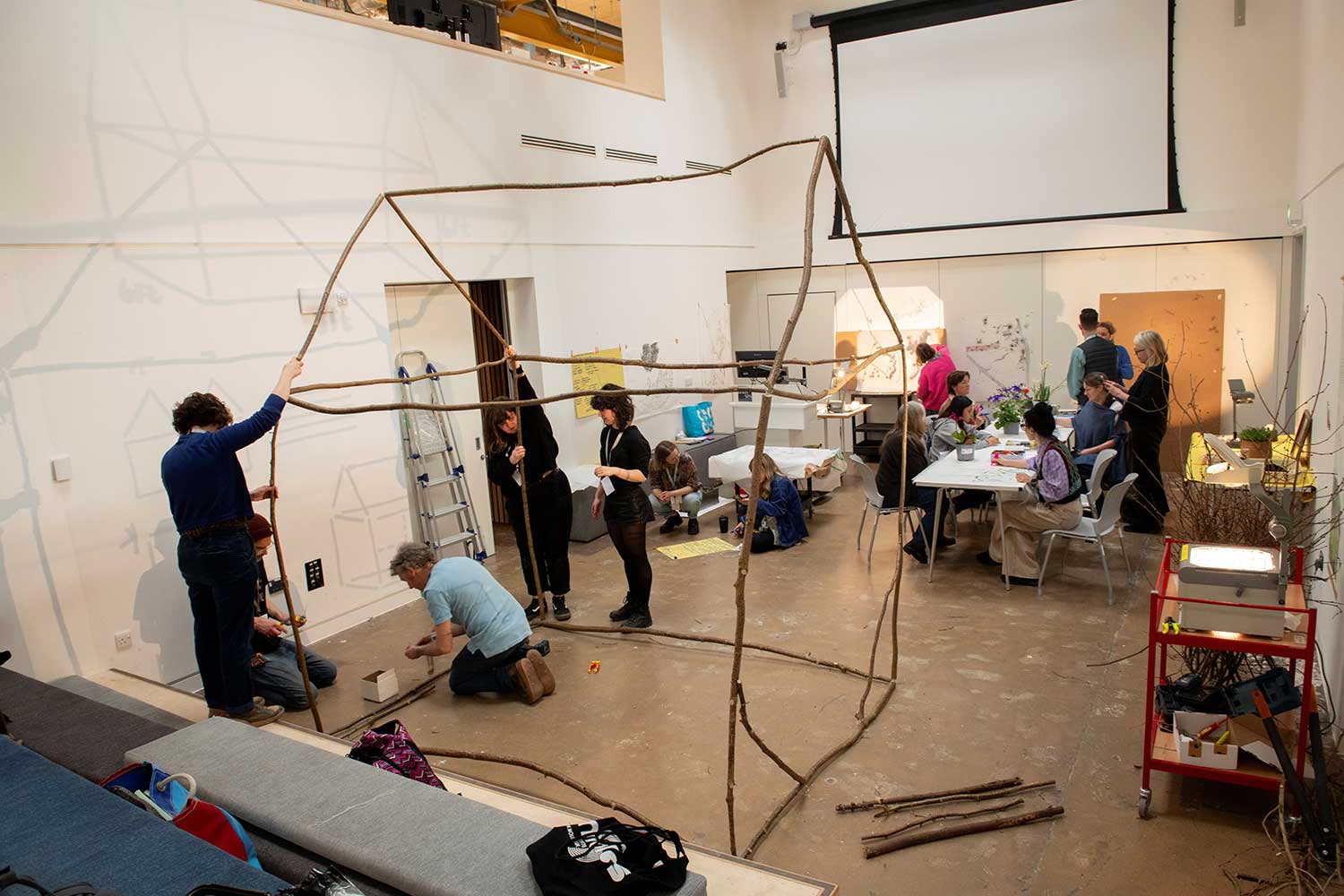 A group of people in a workshop creating a large structure out of branches