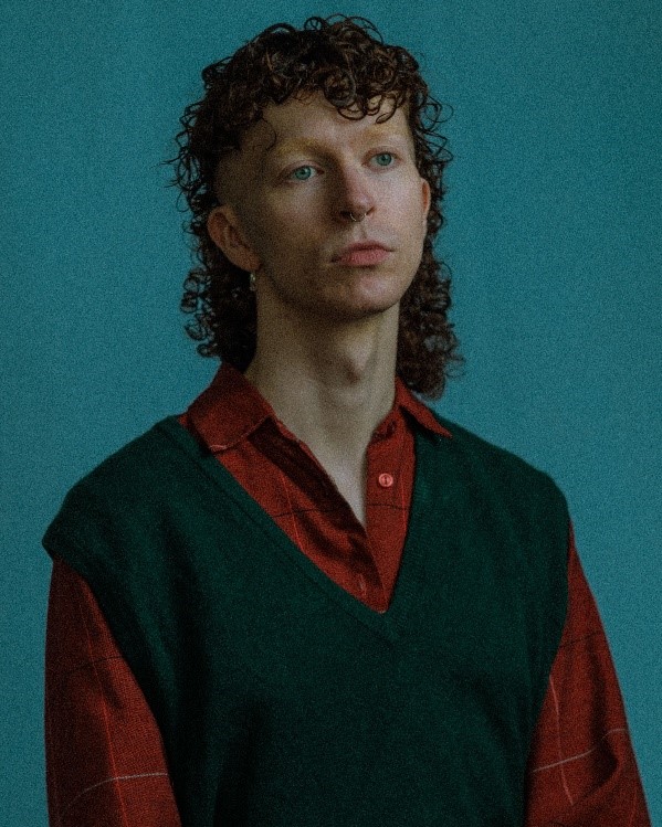 A headshot for a person wearing a red shirt and black sweater